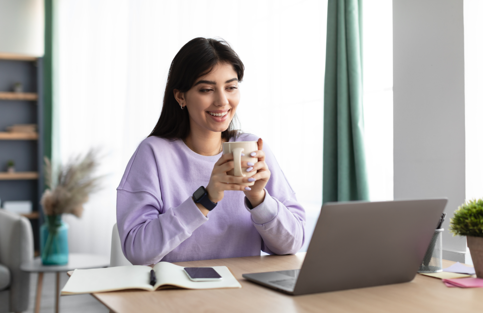 Woman using a laptop at a desk beside a notebook